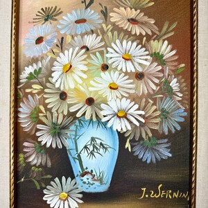 May include: A painting of a bouquet of white daisies in a blue and white vase with a bamboo design. The vase is sitting on a brown surface. The painting is signed "J.Wernin" in the lower right corner.