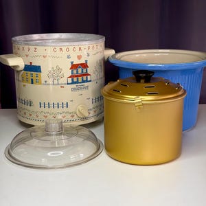 May include: A collection of vintage slow cookers in various colors. The main cooker is cream-colored with a house design and the text "Crock-Pot". A gold-colored cooker and a blue pot are also visible, along with a clear glass lid.