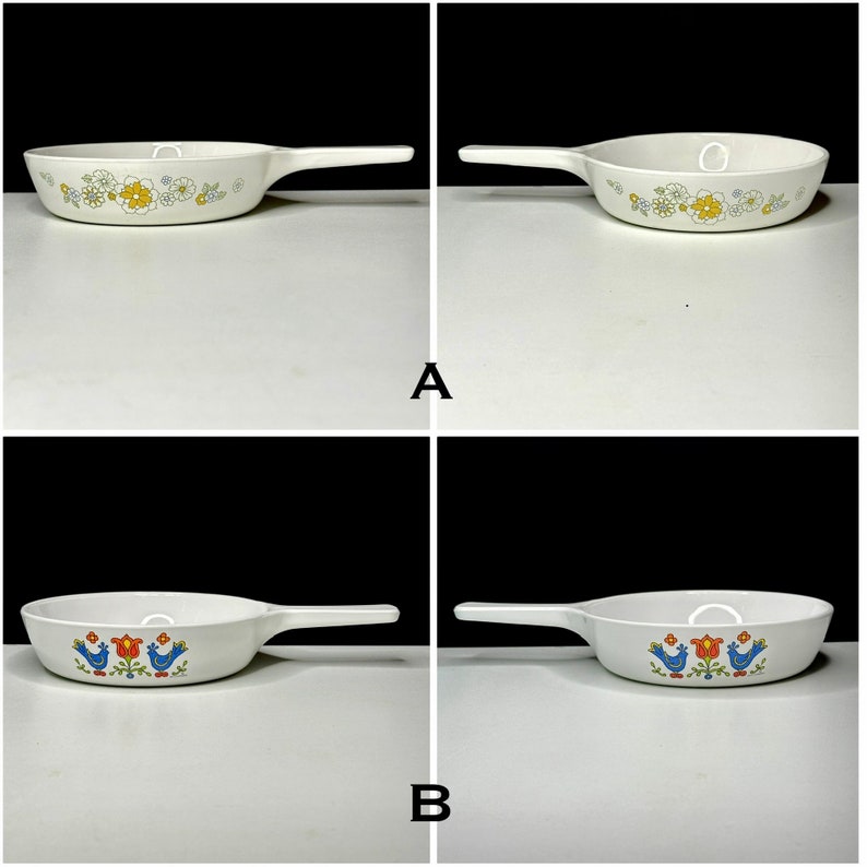 May include: Two vintage white cast iron skillets with different floral patterns. The top skillet has a yellow and white floral pattern. The bottom skillet has a blue bird and flower pattern.