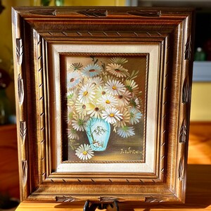 May include: A framed painting of a bouquet of white daisies in a blue vase. The painting is signed "J. Swernin".
