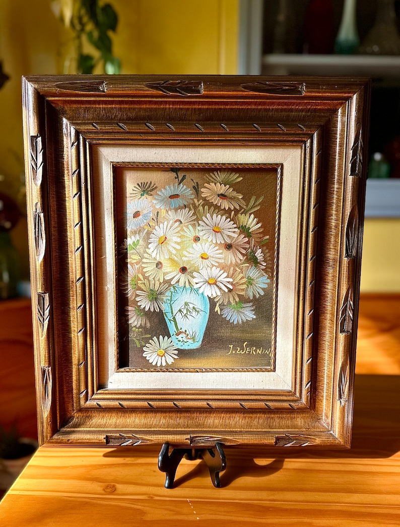 May include: A framed painting of a bouquet of white daisies in a blue vase. The painting is signed "J. Swernin".