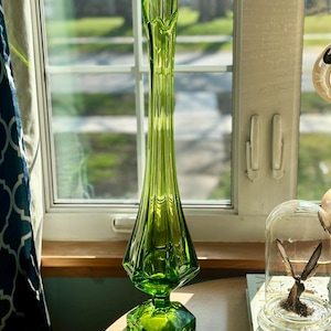 May include: A tall, green glass vase with a flared top and a hexagonal base. The vase has a textured, ribbed design.