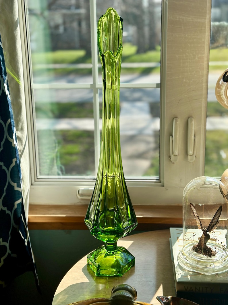 May include: A tall, green glass vase with a flared top and a hexagonal base. The vase has a textured, ribbed design.