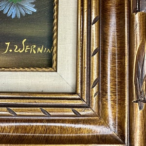May include: A framed painting of a bouquet of flowers with a dark background. The frame is a dark brown wood with gold accents and a carved design. The painting is signed "J.W. Sernin".