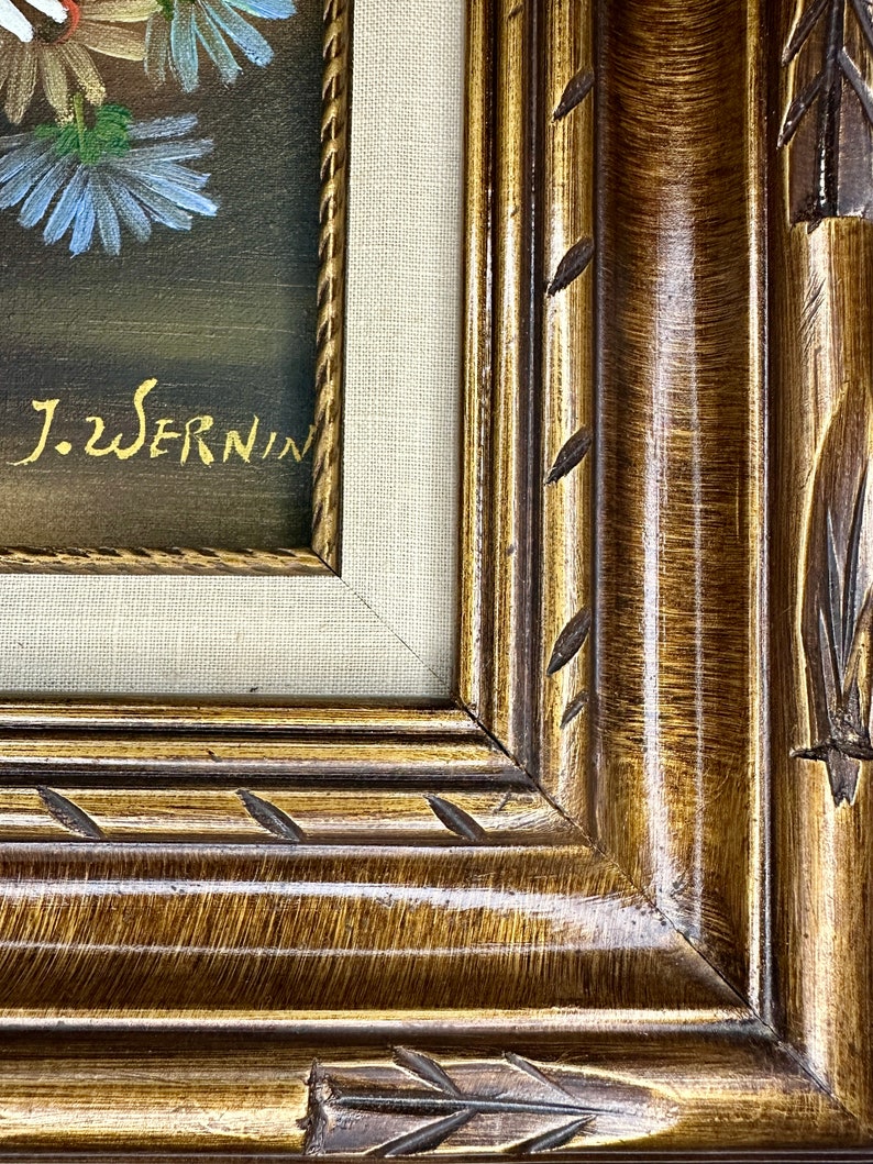 May include: A framed painting of a bouquet of flowers with a dark background. The frame is a dark brown wood with gold accents and a carved design. The painting is signed "J.W. Sernin".