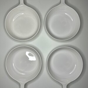 May include: Four white ceramic baking dishes with handles. The dishes are empty and arranged in a square pattern.