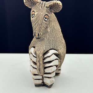 May include: A ceramic sculpture of a brown animal with large ears and a segmented body. The animal has white eyes and a textured surface.