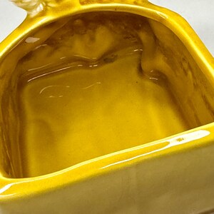 May include: A close-up of a yellow ceramic dish with a bird-shaped handle. The dish has a rectangular shape with rounded corners and a glossy finish. The interior is a darker shade of yellow.
