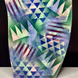 May include: A ceramic vase with a geometric pattern in shades of blue, green, and pink. The vase has a curved, rectangular shape.