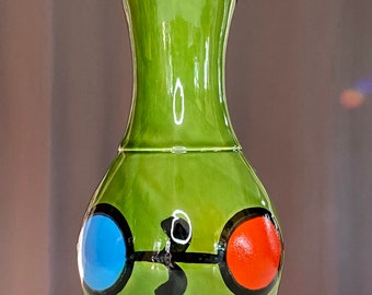 May include: A green ceramic vase with a wide base and a narrow neck. The vase has a black, blue, and red design on the front.
