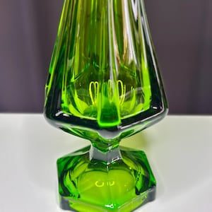 May include: A green glass vase with a flared, trumpet-shaped body and a hexagonal base.
