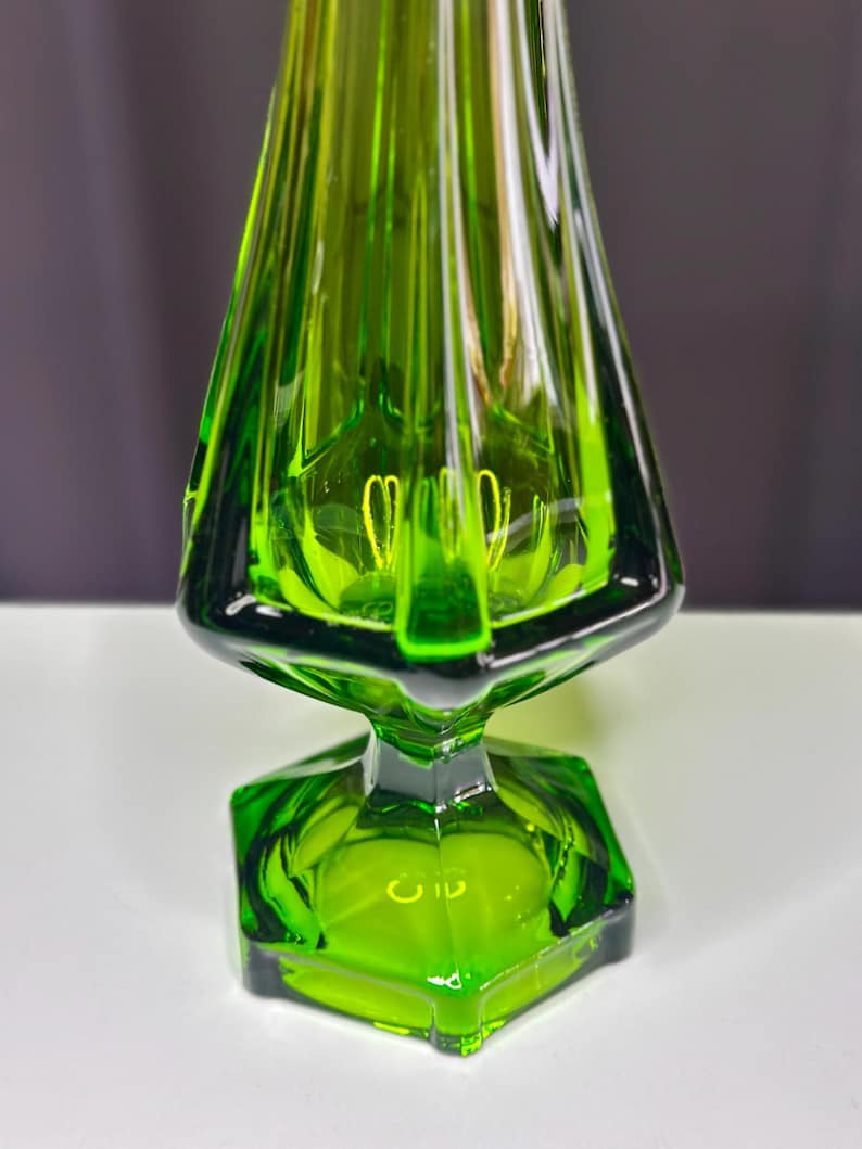 May include: A green glass vase with a flared, trumpet-shaped body and a hexagonal base.