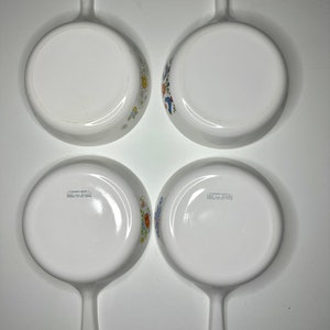 May include: Set of four white ceramic baking dishes with blue and yellow floral designs. Each dish has a single handle and the words "Corning Ware" and "Made in USA" are printed on the bottom.