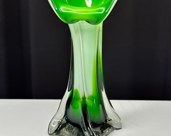 May include: A green and white glass vase with a unique, flared design. The vase has a wide, open top and a narrow base.