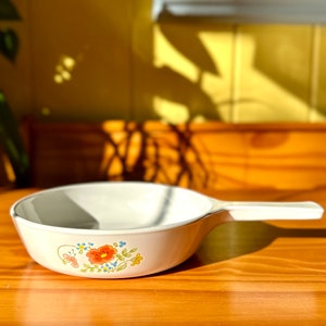 May include: White ceramic saucepan with a floral design featuring orange, red, blue, and green flowers. The saucepan has a white handle.