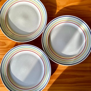 May include: Three white ceramic plates with colorful stripes. The plates have a blue, green, yellow, and red stripe pattern.