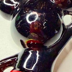 K&ouml;nnte beinhalten: Gl&auml;nzende schwarze Mickey Mouse-Figur mit rotem Unterteil. Die Figur hat gro&szlig;e, runde Ohren und einen fr&ouml;hlichen Ausdruck. Die Figur ist eine klassische Disney-Figur.