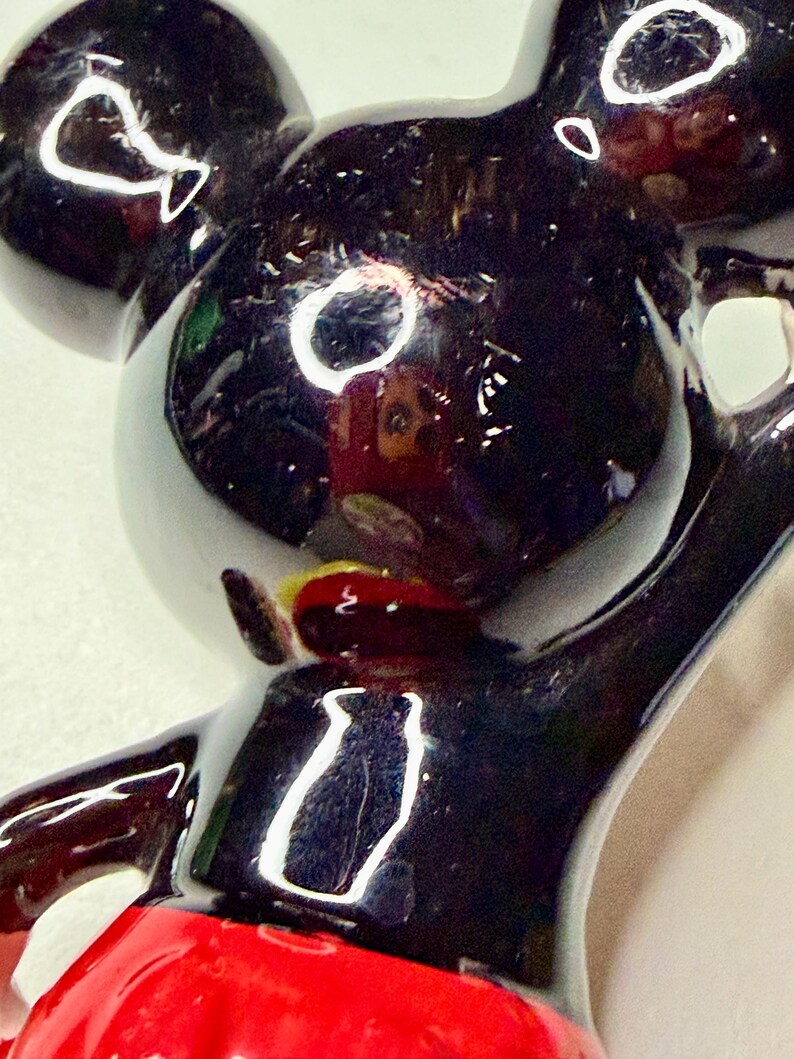 K&ouml;nnte beinhalten: Gl&auml;nzende schwarze Mickey Mouse-Figur mit rotem Unterteil. Die Figur hat gro&szlig;e, runde Ohren und einen fr&ouml;hlichen Ausdruck. Die Figur ist eine klassische Disney-Figur.