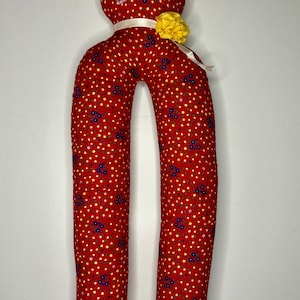 May include: A red fabric cat-shaped pillow with a yellow flower on its head. The pillow is covered in a red fabric with a pattern of small yellow stars and blue flowers.