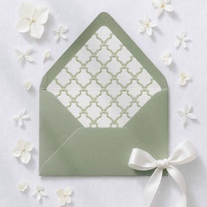 May include: An open sage green envelope with a white patterned interior and a white satin bow. White flowers are scattered around the envelope, creating a delicate and elegant composition. The envelope is likely for invitations or stationery.