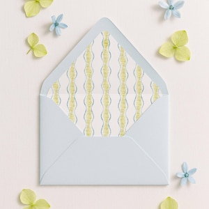 May include: A light blue envelope with a patterned interior, decorated with small blue and yellow flowers. The envelope's interior features a white background with vertical yellow and blue wavy lines.
