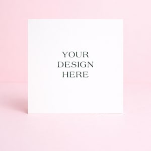 May include: A white square card with the text "YOUR DESIGN HERE" in a dark green font. The card is centered on a light pink background, creating a clean and minimalist aesthetic. Ideal for showcasing custom designs.