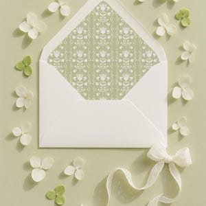 a white envelope with a green floral pattern, surrounded by white flowers and a white ribbon.