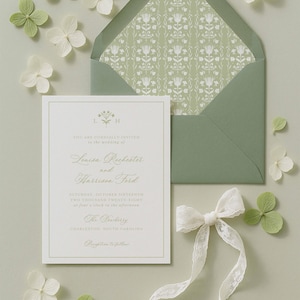 a wedding invitation card with a green envelope, white flowers, and a white ribbon.