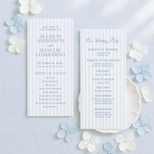 May include: Wedding invitation suite featuring two light blue striped cards with event details and names. The cards are surrounded by white and light blue flowers, creating a soft, elegant aesthetic.
