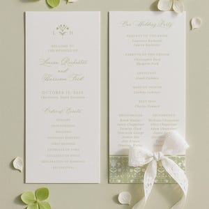 a wedding invitation card with a white background and green leaves. The card is placed on a light green background with white flowers scattered around it.