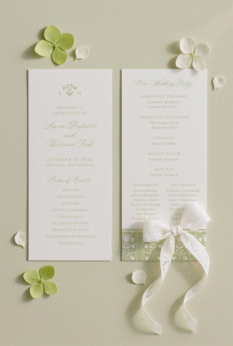 a wedding invitation card with a white background and green leaves. The card is placed on a light green background with white flowers scattered around it.