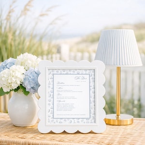 May include: A white scalloped picture frame containing a printed bar menu titled The Bar, featuring a light blue patterned border with small illustrations. The menu lists various beverage categories including Bubbles, Wine, Beer, and Spirits.