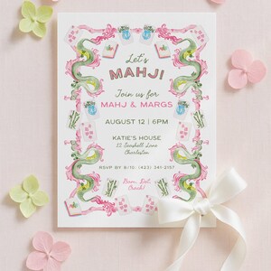 May include: A watercolour invitation for a Mahjong party. The invitation features the text "Let's MAHJ!" and "Join us for MAHJ & MARGS". The design includes green dragons, pink accents, and Mahjong tiles. Pink and green flowers and a white ribbon complete the design.