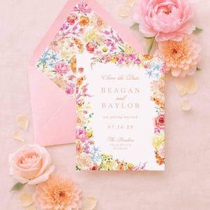 Puede incluir: Un conjunto de invitaciones de boda rosa con un diseño floral. La invitación dice "Save the Date" con los nombres "Reagan and Baylor" y la fecha "07.15.28". Un sobre con un interior floral y varias flores rodean la invitación.