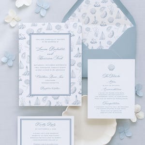 May include: A wedding invitation suite featuring a light blue envelope with a nautical pattern, a main invitation, a details card, and an RSVP card. The stationery displays blue ink text and illustrations of lighthouses, sailboats, and seashells.