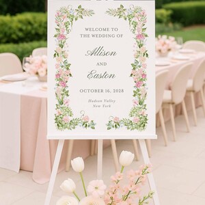 Editable watercolor floral wedding welcome sign on an easel beside pastel flowers at an elegant outdoor ceremony.