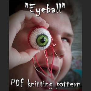 May include: A knitted eyeball with a green iris and red yarn attached. The text "Eyeball!" is written above the eyeball. The text "PDF knitting pattern" is written below the eyeball.
