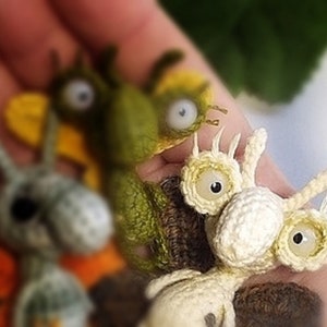 K&ouml;nnte beinhalten: Drei geh&auml;kelte Amigurumi-Spielzeuge, jedes mit gro&szlig;en Augen. Das erste ist gr&uuml;n mit gelben Fl&uuml;geln, das zweite ist grau mit orangefarbenen Fl&uuml;geln und das dritte ist wei&szlig; mit einer braunen Basis.