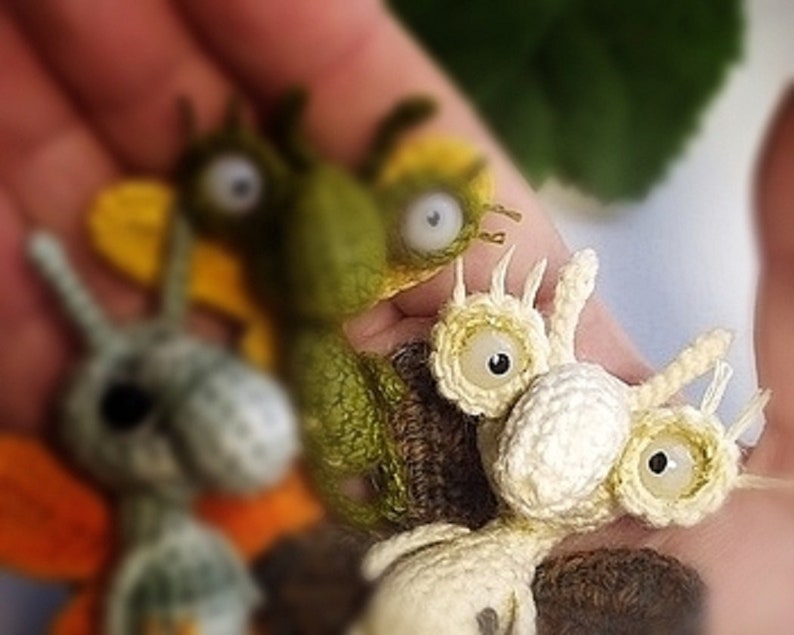K&ouml;nnte beinhalten: Drei geh&auml;kelte Amigurumi-Spielzeuge, jedes mit gro&szlig;en Augen. Das erste ist gr&uuml;n mit gelben Fl&uuml;geln, das zweite ist grau mit orangefarbenen Fl&uuml;geln und das dritte ist wei&szlig; mit einer braunen Basis.