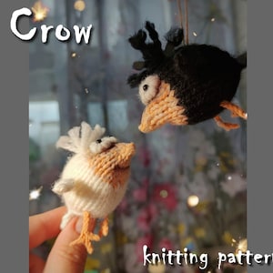 May include: Knitting pattern for a black and white crow with orange beak and feet. The crow is holding a white and orange bird with a black eye.