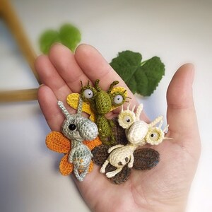 K&ouml;nnte beinhalten: Vier geh&auml;kelte Amigurumi-Kreaturen mit gro&szlig;en Augen und Fl&uuml;geln. Die Kreaturen sind gr&uuml;n, grau, wei&szlig; und braun.