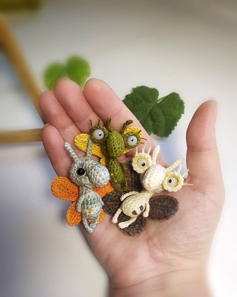 K&ouml;nnte beinhalten: Vier geh&auml;kelte Amigurumi-Kreaturen mit gro&szlig;en Augen und Fl&uuml;geln. Die Kreaturen sind gr&uuml;n, grau, wei&szlig; und braun.