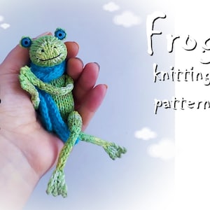 Może przedstawiać: Zielona dziana żaba w niebieskim szaliku. Żaba siedzi w dłoni na białym tle. Tekst "Frog knitting pattern" jest napisany czarnym kolorem po prawej stronie obrazu.