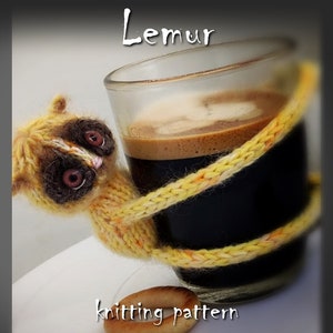 May include: A knitted lemur toy in yellow and orange hues is wrapped around a glass of coffee. The lemur has large, pink eyes and a brown nose. The text "Lemur knitting pattern" is visible below the image.