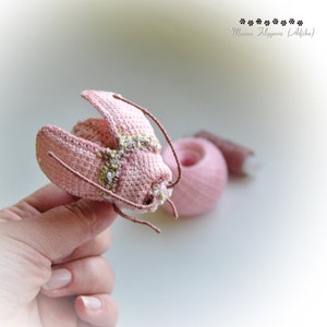 May include: A crocheted pink butterfly with brown wire antennae. The butterfly has a detailed design with white and green accents.