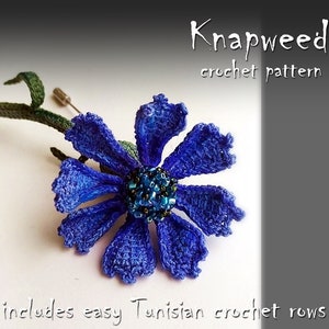 May include: A crocheted blue knapweed flower with a green stem and a pin attached. The flower is made with a Tunisian crochet technique. The text "Knapweed crochet pattern" and "includes easy Tunisian crochet rows" is visible in the image.