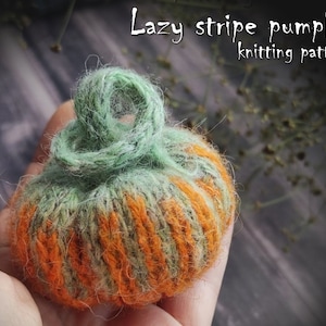 May include: A knitted pumpkin with green and orange stripes. The pumpkin has a green stem and is held in a hand. The text "Lazy stripe pumpkin knitting pattern" is above the pumpkin.