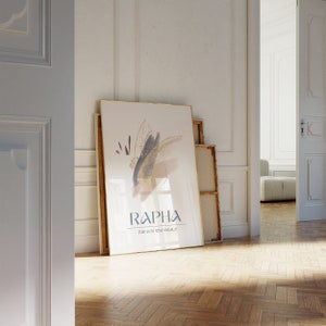 May include: A framed art print with gold trim, leaning against a wall. The artwork features abstract brushstrokes in navy, gold, and beige, with the word "RAPHA" and the phrase "THE GOD WHO HEALS" in navy text.