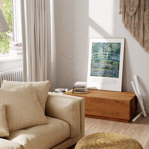 Puede incluir: Una sala de estar con un sof&aacute; beige, una mesa de caf&eacute; de madera y una impresi&oacute;n enmarcada de una pintura de un puente sobre un estanque. La impresi&oacute;n est&aacute; colgada en una pared blanca. El sof&aacute; tiene dos almohadas, una beige y una blanca. La mesa de caf&eacute; tiene una pila de libros encima. El suelo es de madera.