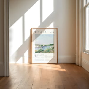 May include: A framed print of Psalm 23, featuring a landscape painting with a river and greenery. The print has a wooden frame and is leaning against a white wall. The text "Psalm 23" is at the top, with "A Psalm of David" below.